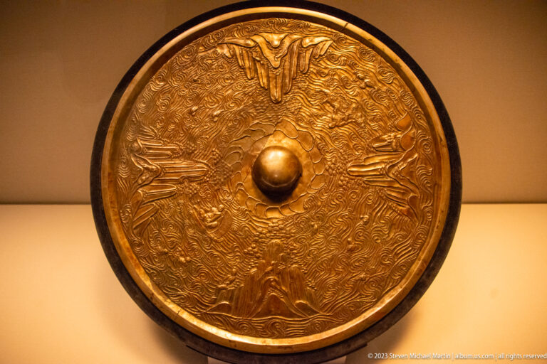 Circular mirror back with central boss, four island motifs, figures, animals, and concentric waves.