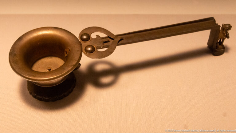 Bronze ladle with deep bowl, long straight handle, forked ornament, and hooked end.