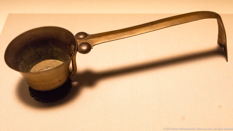 Deep bronze cup with a long flat handle ending in a sharp downward hook.