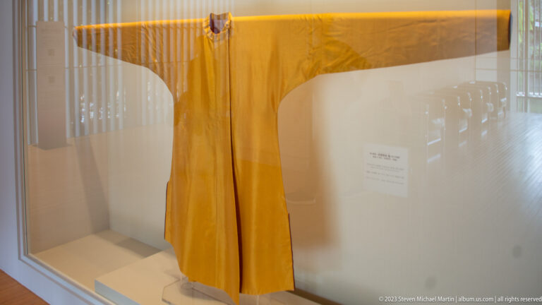 Large yellow robe or ceremonial garment hanging in a glass museum case.