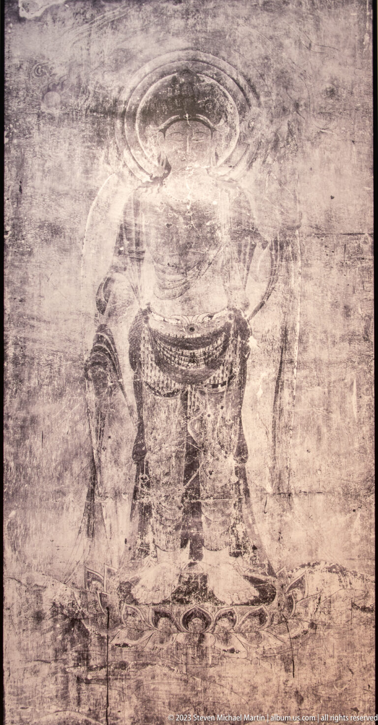 Large faded standing Buddhist figure with a broad halo on a worn mural surface.