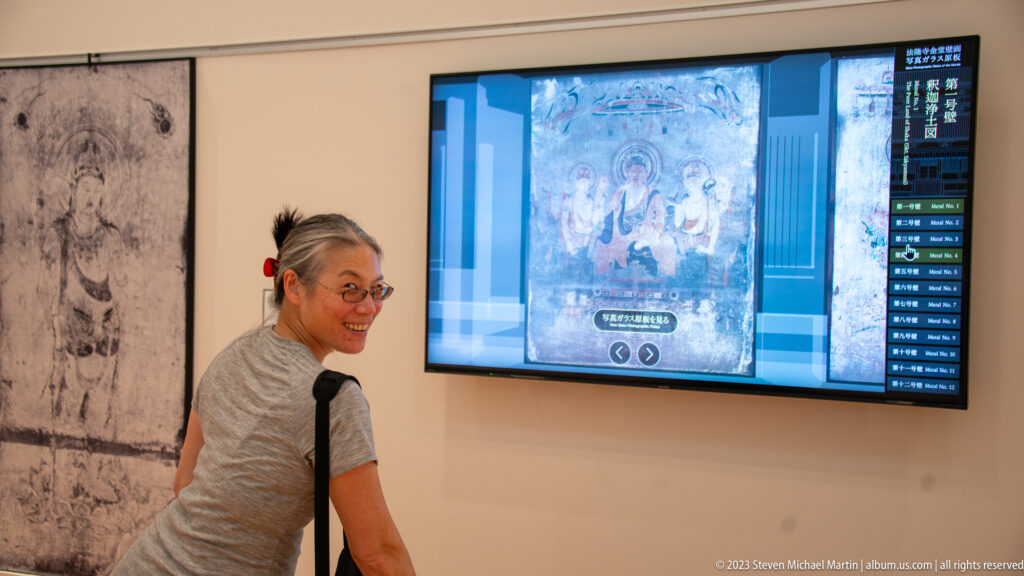Visitor beside an interactive screen displaying a reconstructed Buddhist mural, with the faded original visible nearby.