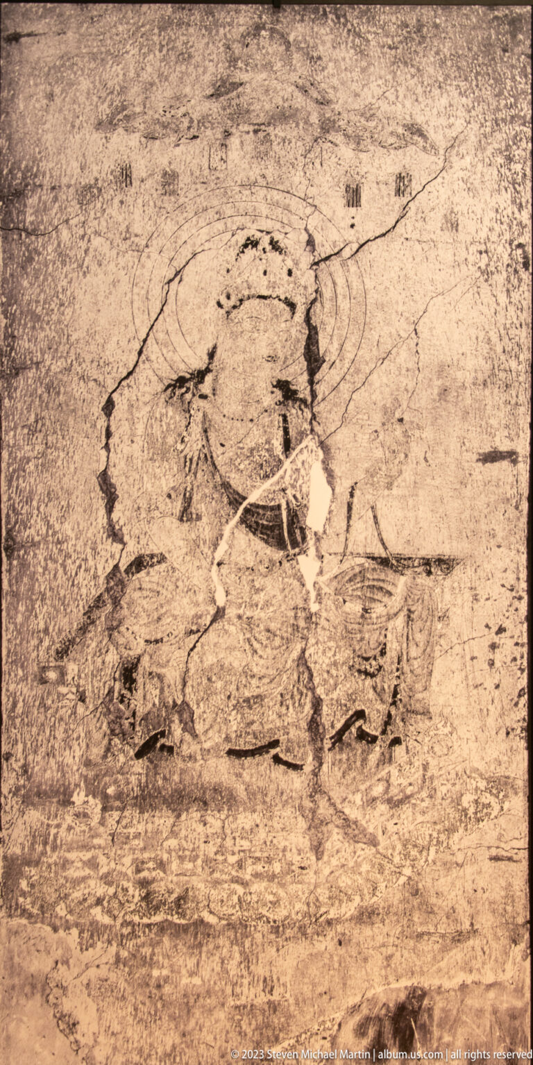 Faded seated haloed figure with bent arms on a pale, heavily worn mural.