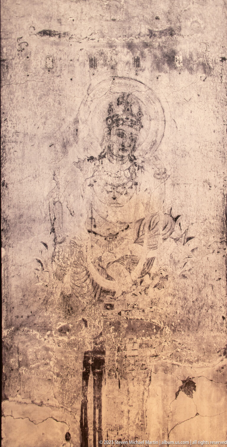 Faint seated haloed Buddhist figure on a lotus pedestal in a heavily worn mural.