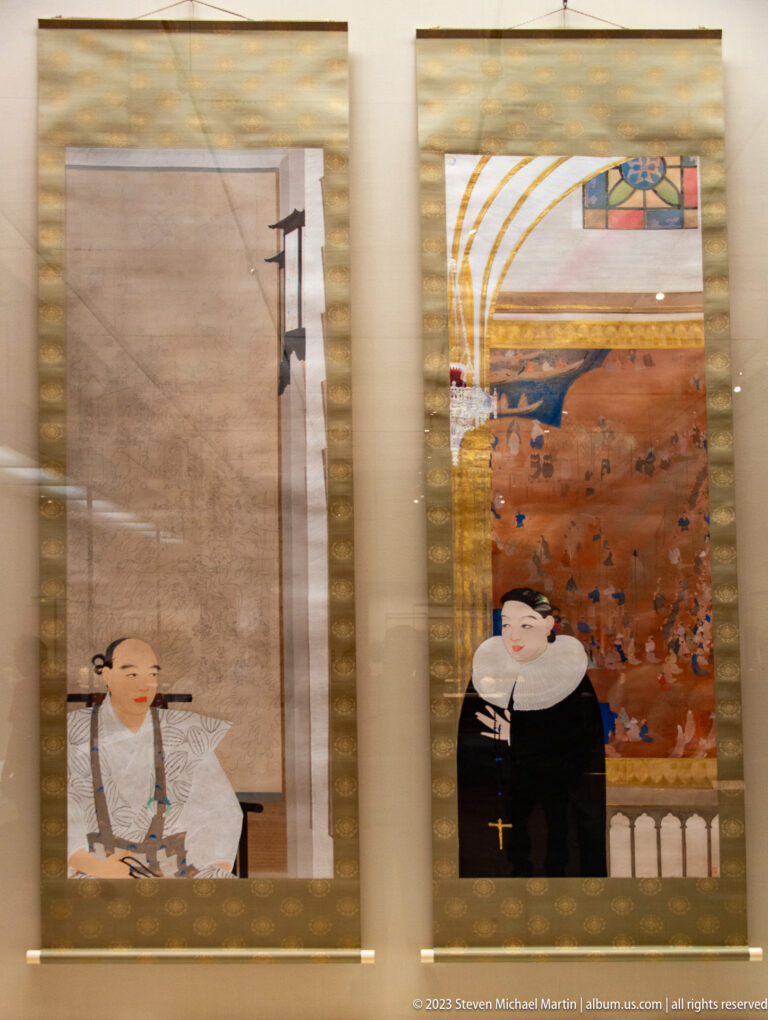 Two hanging scroll portraits, one of a Japanese man and one of a European cleric in black.