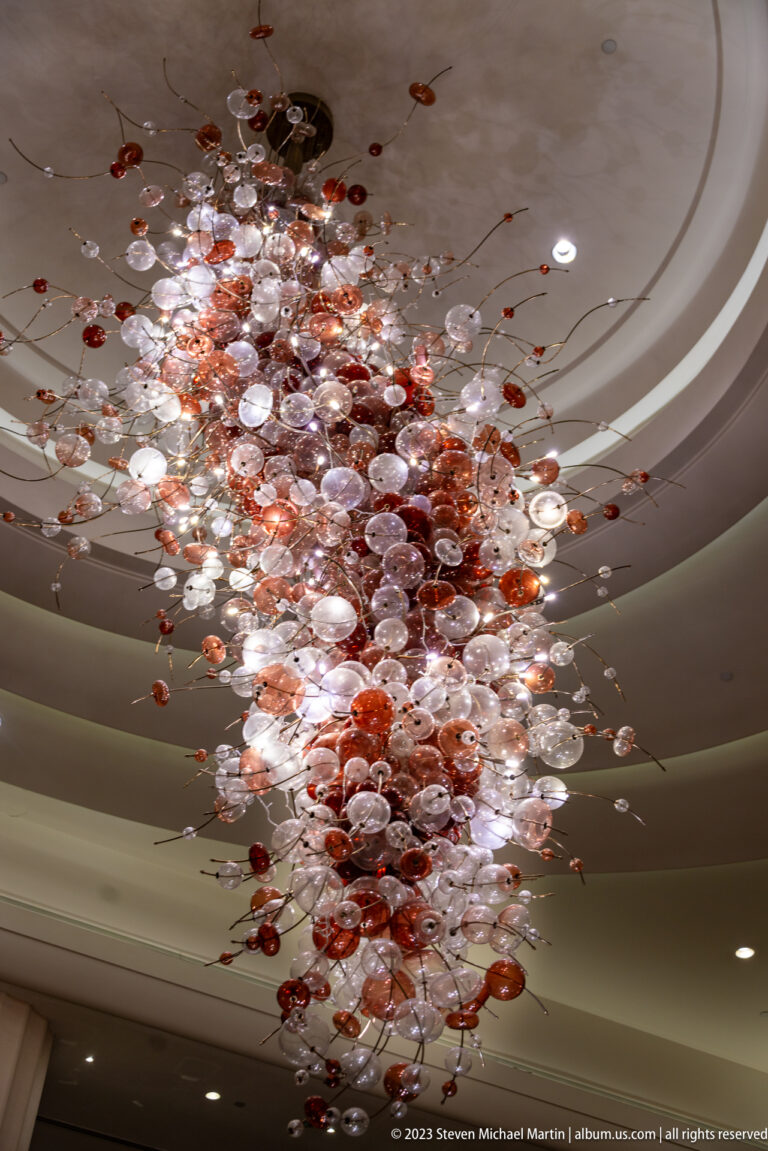 Suspended red and clear glass forms clustered beneath a curved ceiling.