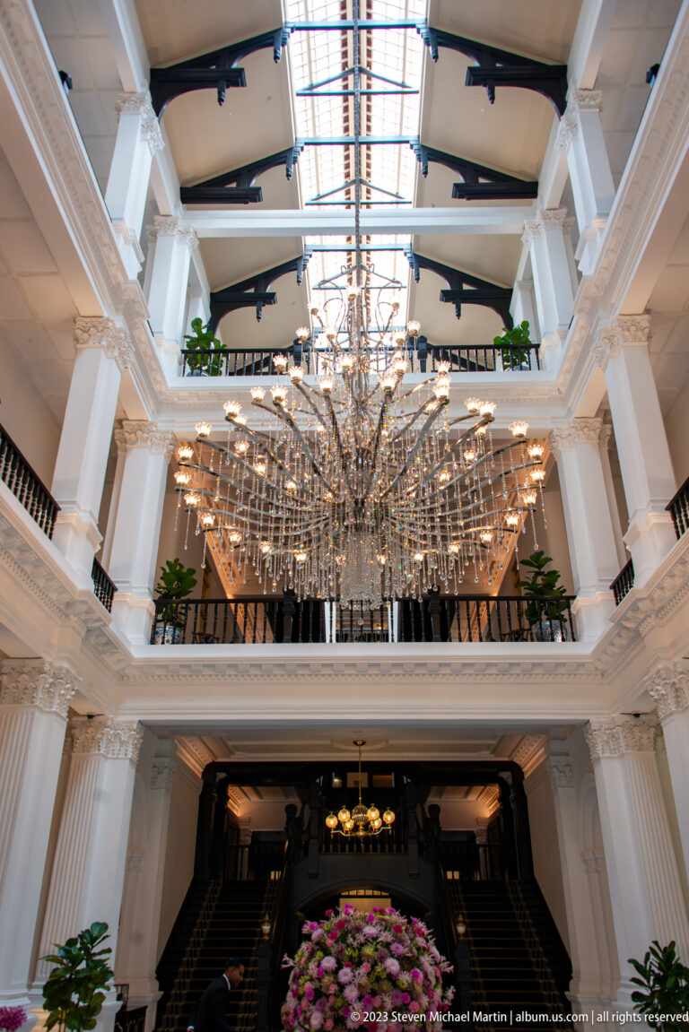 Large branching chandelier suspended beneath a glazed atrium roof above white balconies.