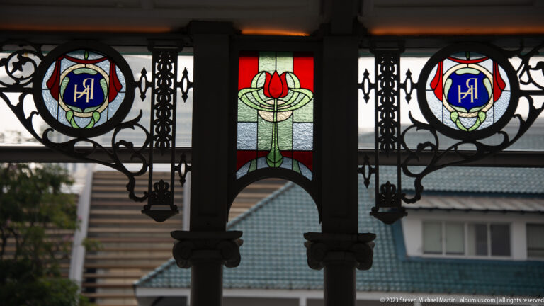 Stained-glass shields and floral motif set within a black wrought-iron veranda screen.