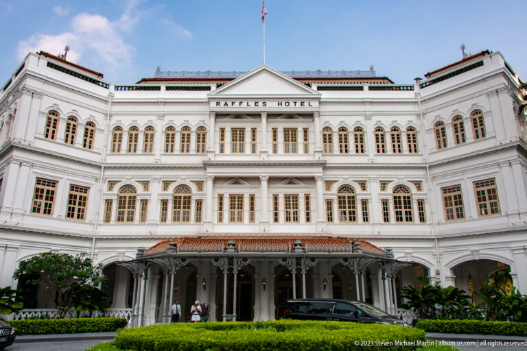 White curved façade of Raffles Hotel with arcades, shuttered windows, and red-tiled roof.