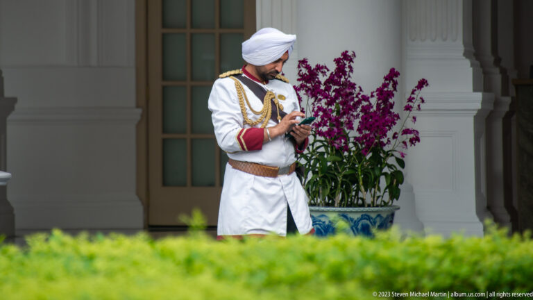 Uniformed hotel staff member in white ceremonial dress beside purple orchids.