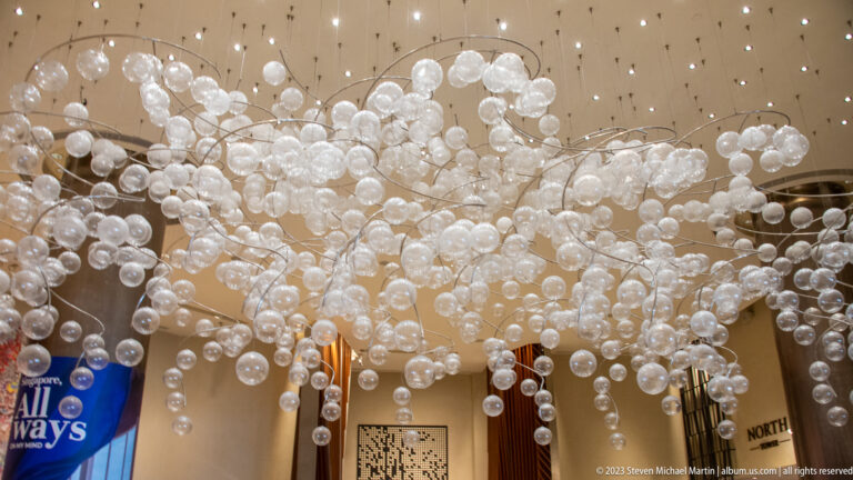 Ceiling installation of many clear glass globes branching above an indoor concourse.