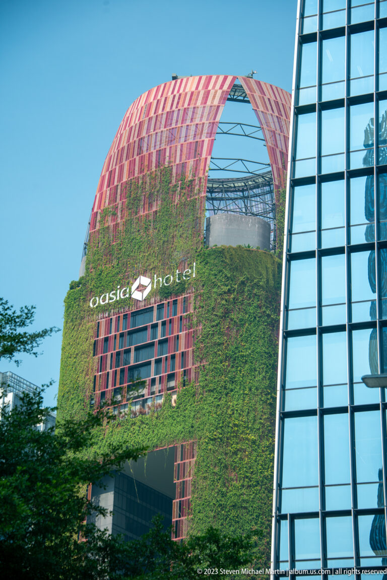 Oasia Hotel Downtown with red lattice crown and green plant-covered façade.