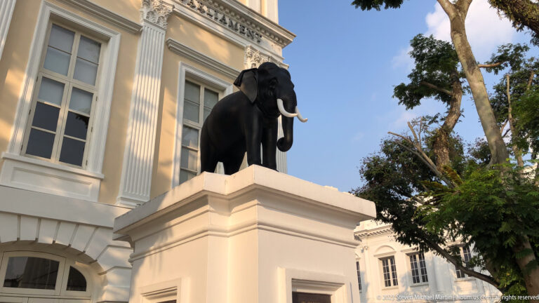 Black elephant sculpture with pale tusks on a white pedestal beside the museum.