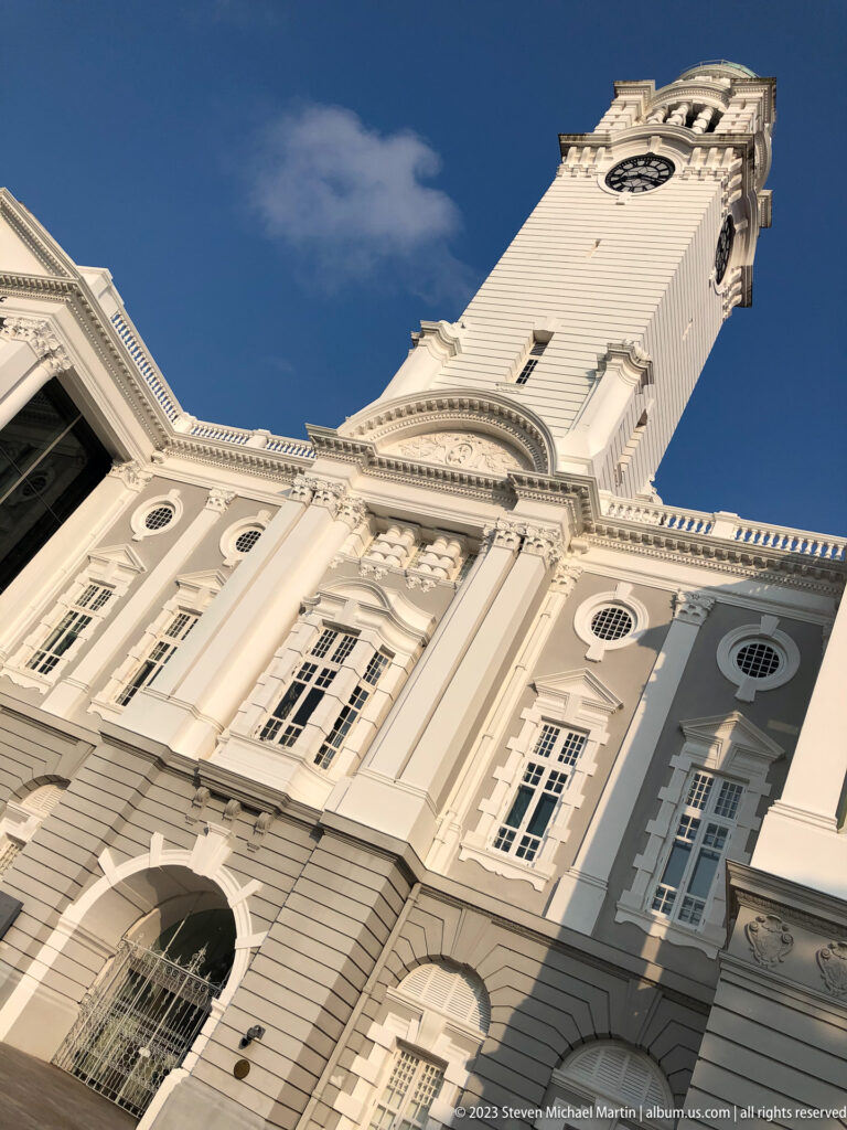 Steep upward view of the white clock tower and classical façade of Victoria Theatre.