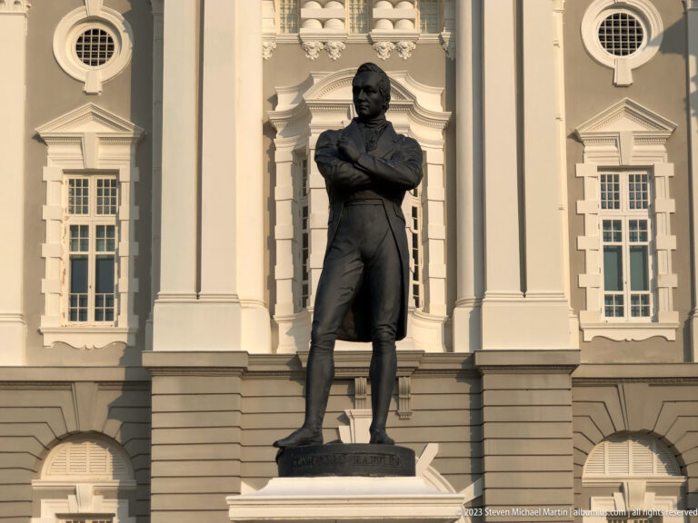 Bronze statue of Sir Stamford Raffles before the white façade of Victoria Theatre.