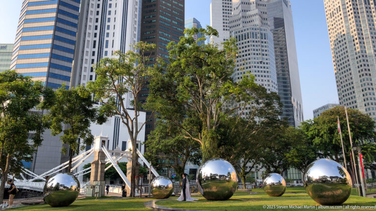 Several polished mirror-like metal spheres arranged on a lawn among trees and towers.