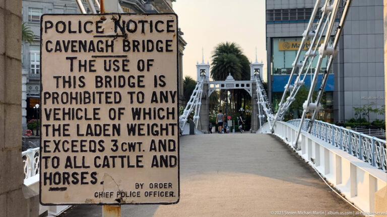 Old Cavenagh Bridge notice sign beside the white suspension bridge entrance.