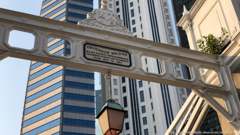 Decorative iron crossbeam and plaque on Cavenagh Bridge with office towers behind.