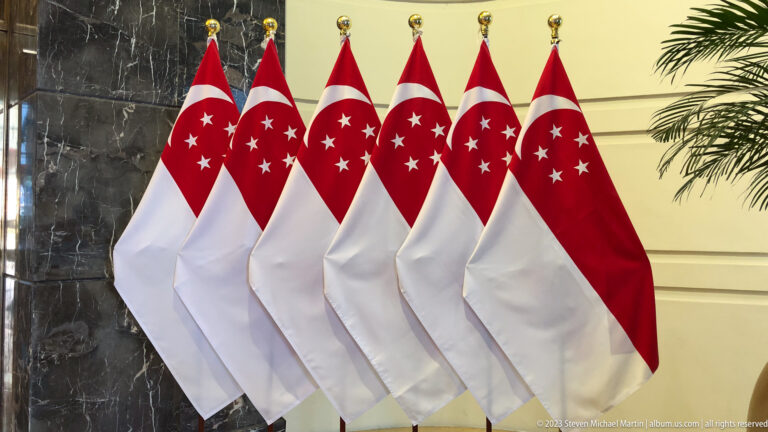 Several Singapore flags arranged in a row beside a marble wall.
