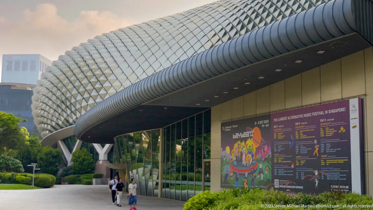 Esplanade entrance with glass walls, broad canopy, spiked roof, and pedestrians.