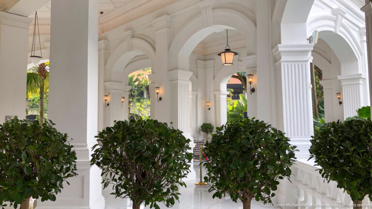 White arched hotel veranda with fluted columns, lanterns, and potted shrubs.