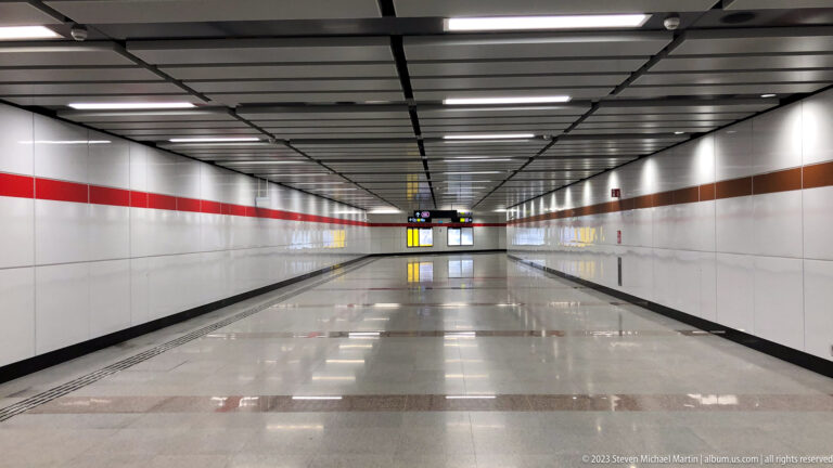 Long empty MRT corridor with tiled walls, horizontal stripes, and reflective floor.