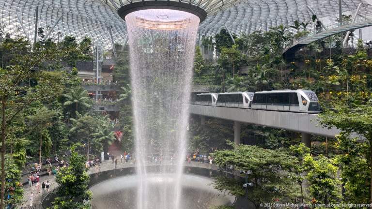 Rain Vortex beside an elevated airport train passing through Jewel Changi Airport.