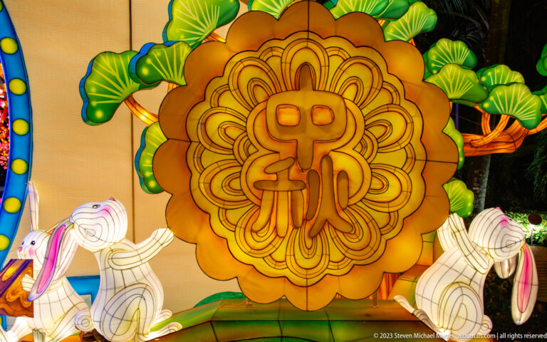 Golden mooncake-shaped lantern with a central Chinese character, flanked by white rabbits and green leaves.