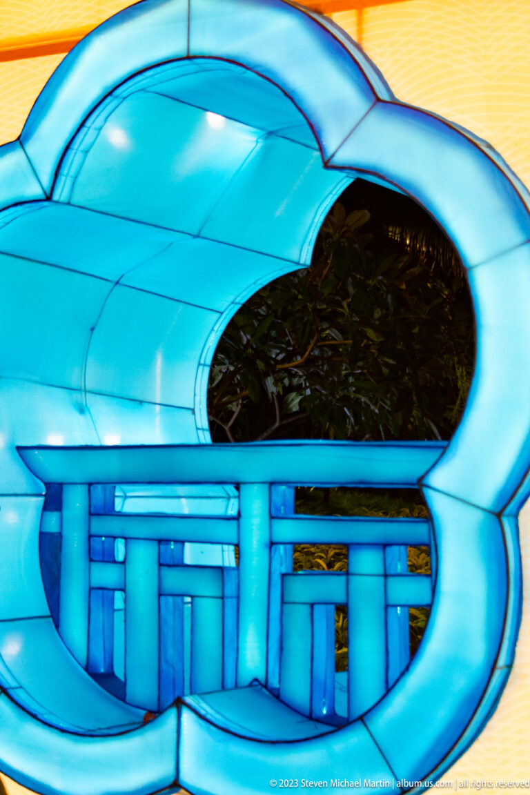 Blue illuminated lantern structure with a rounded opening, white bands, posts, and rail-like details.