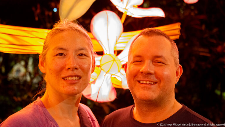 Two smiling adult visitors posing together at night in front of bright orange-and-white lantern decorations.