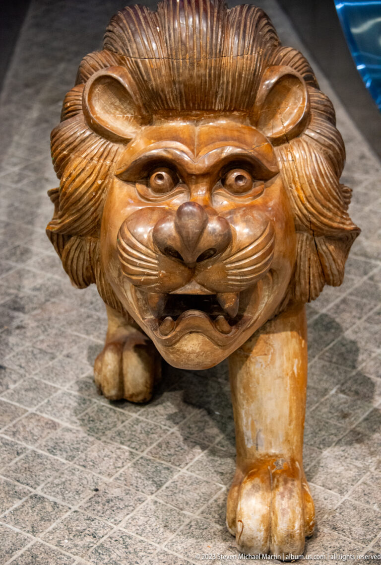 Front-facing brown guardian-lion sculpture with broad mane, open mouth, and sturdy legs.