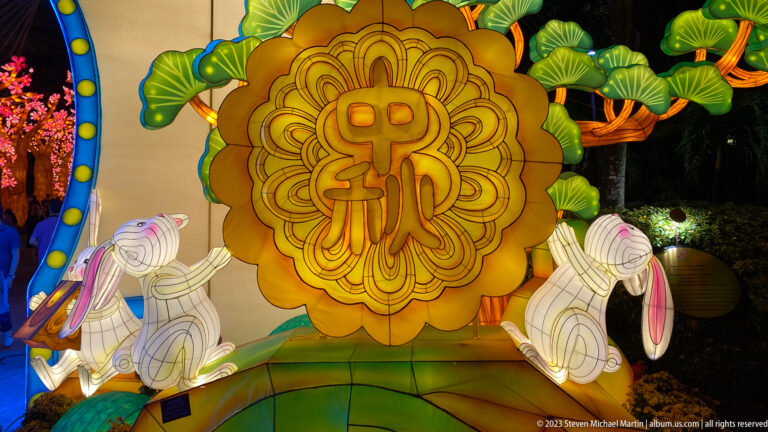 Golden mooncake lantern with a Chinese character flanked by two white rabbits.