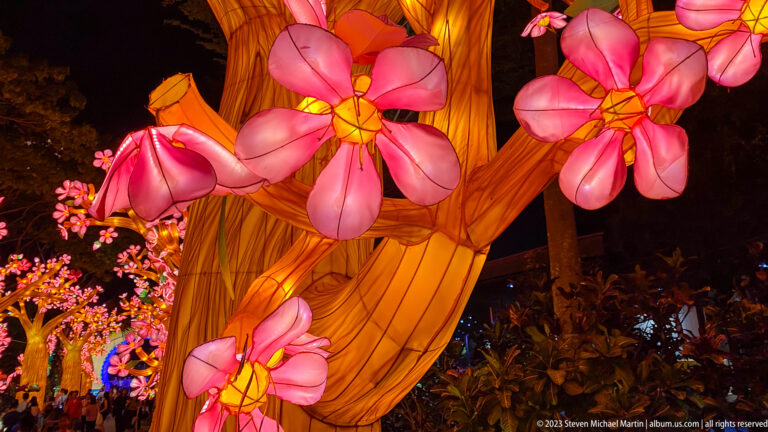 Large pink flower lanterns attached to a glowing amber trunk with smaller trees behind.