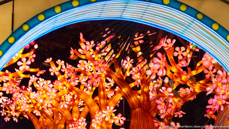 Circular blue-and-yellow gateway framing glowing orange trees covered with pink blossom lanterns.