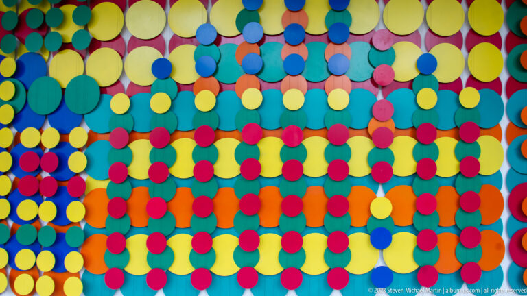 Wall covered with overlapping circular discs in yellow, blue, green, red, orange, and magenta.
