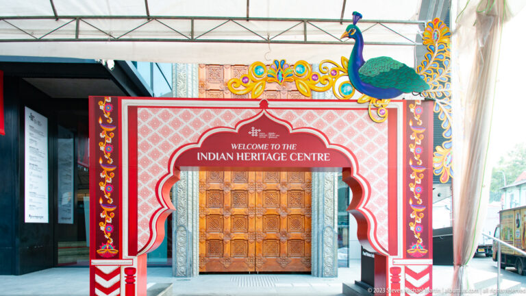 Decorated Indian Heritage Centre entrance frame with floral patterns, peacock crest, and wooden-door image.