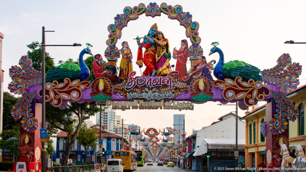 Decorative Deepavali Festival of Lights arch with peacocks and Hindu deities spanning a Little India street.