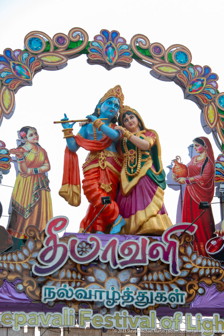 Close view of Krishna with flute beside Radha on a colorful Deepavali street arch.