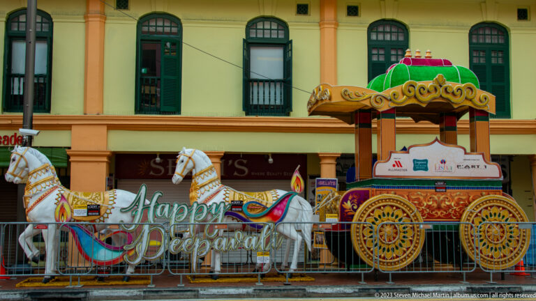 Decorative white horses and gilded carriage beside an illuminated Happy Deepavali greeting.