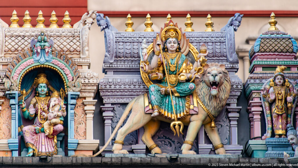 Painted multi-armed Durga seated on a lion in an ornate temple niche with smaller deities.