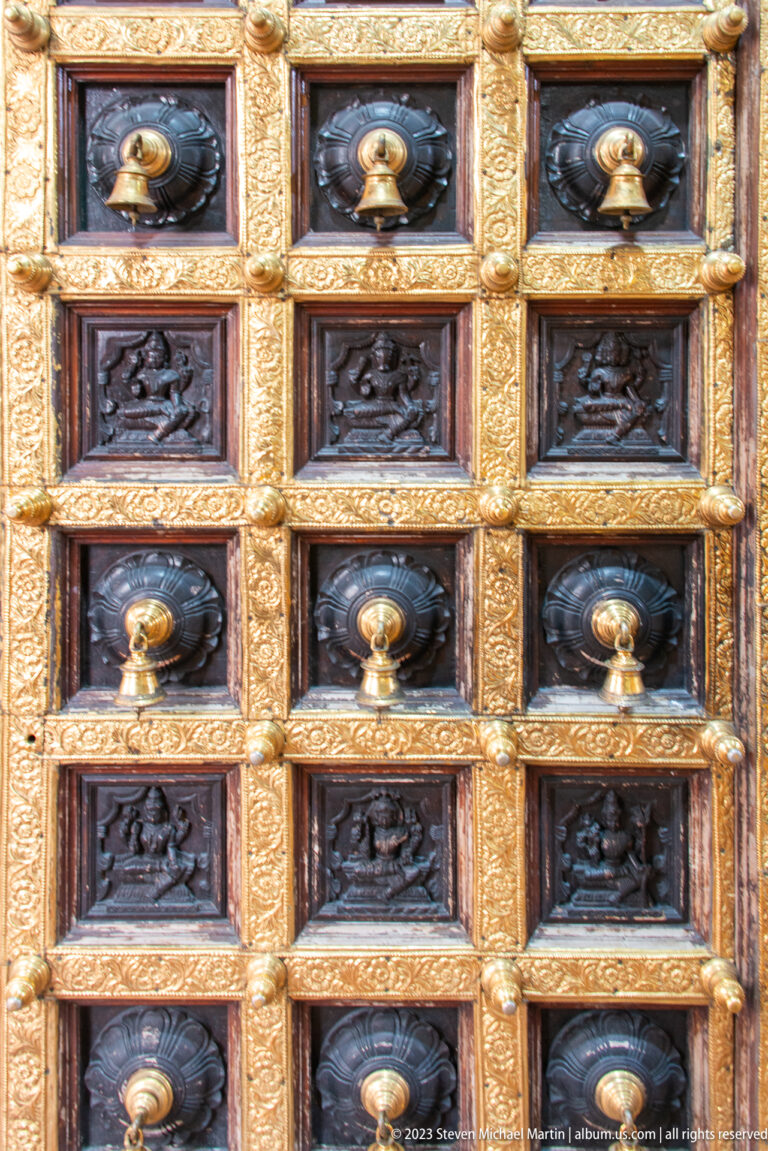 Close view of gilded temple door with carved relief panels and rows of round metal bosses.