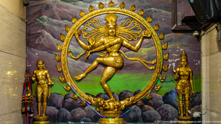 Golden Nataraja dancing within a ring of flames, with one foot raised and attendants beside him.