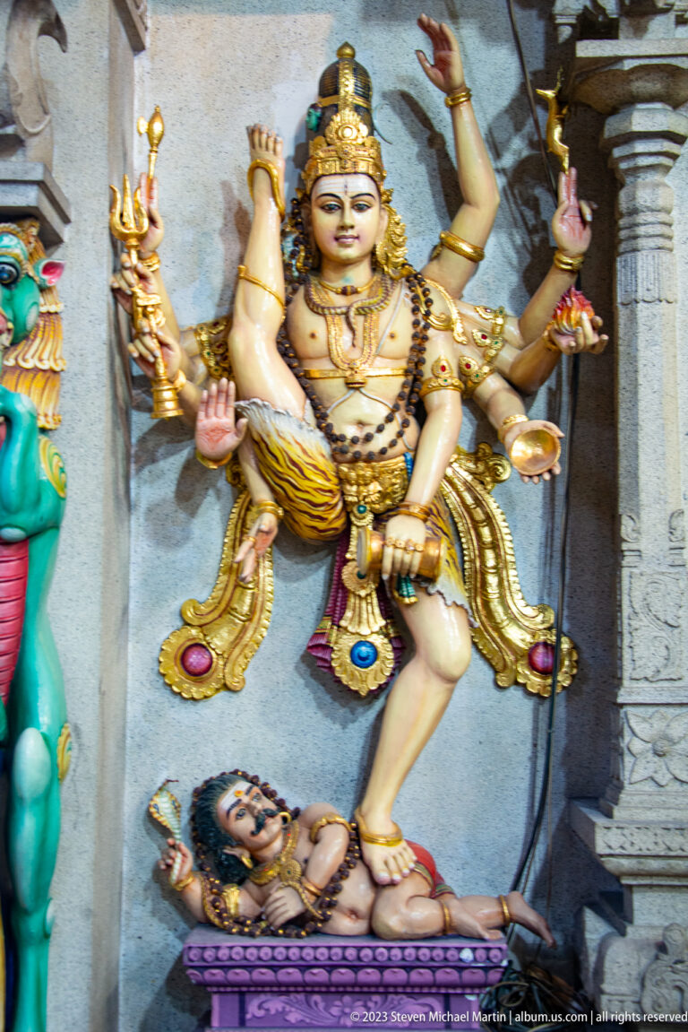 Multi-armed crowned goddess standing over a reclining male figure, with weapons and lotus in her hands.