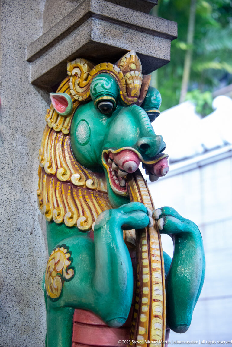 Turquoise yali guardian with gold mane, curled snout, tusks, and open mouth.