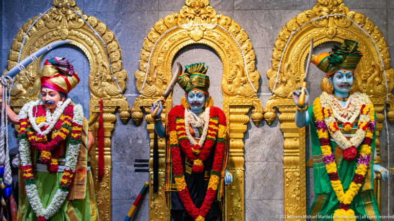 Three garlanded Hindu deities standing beneath separate gilded arches.