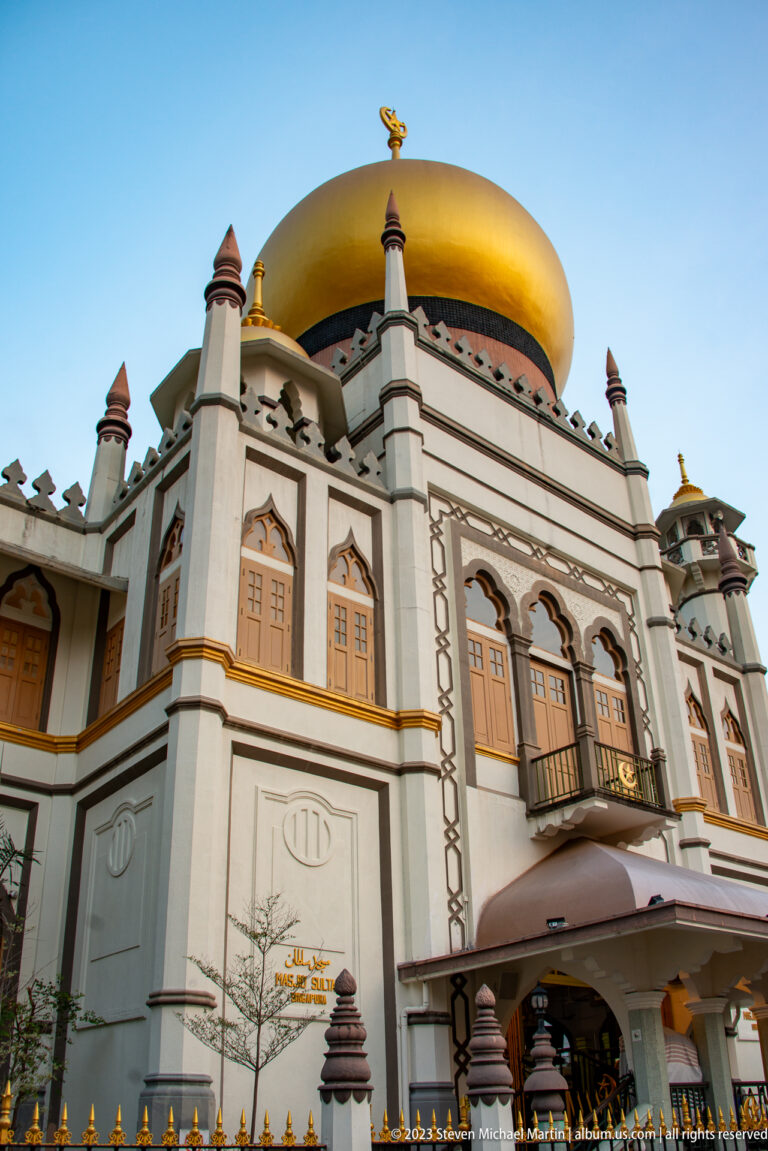 Front façade of Masjid Sultan with golden dome, corner turrets, arched openings, and entrance canopy.