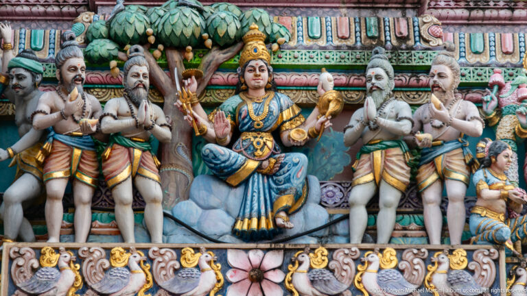 Seated goddess flanked by bearded sages and attendants above a row of bird motifs.