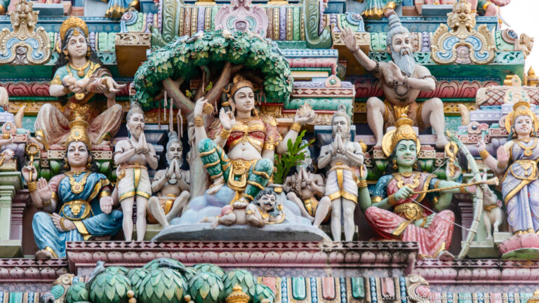 Temple sculpture with seated deities, sages, attendants, and a leafy canopy.