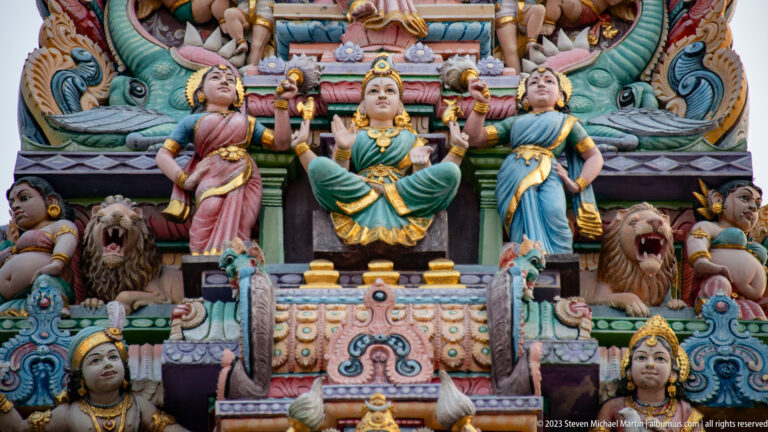 Seated goddess with female attendants and roaring lions on a colorful temple façade.