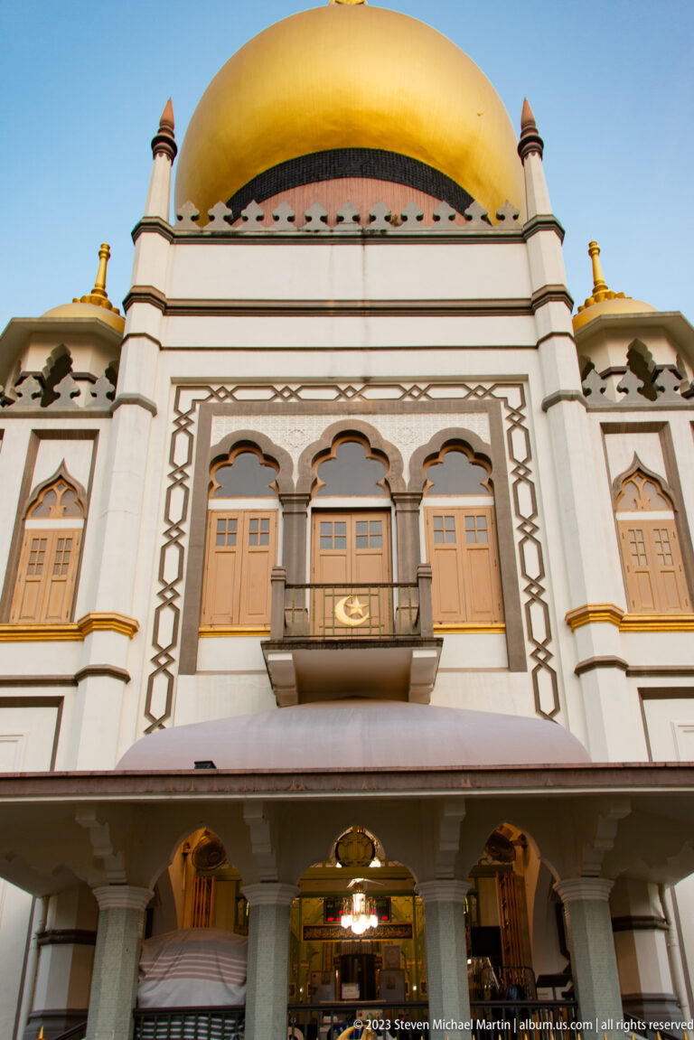 Close frontal view of Masjid Sultan’s golden dome, patterned trim, balcony, shutters, and arched entrance.